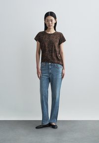Brown leopard print t-shirt with short sleeves; light blue denim jeans featuring scattered white accents; black flat shoes; plain background.
