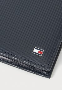 Navy ribbed leather wallet with a silver logo featuring blue, white, and red accents. Smooth texture with reinforced stitching along edges.