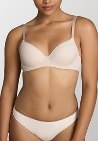 Reggiseno beige senza cuciture con spalline sottili regolabili, coppe sagomate e una fascia morbida sotto il busto, progettato per comfort e supporto.