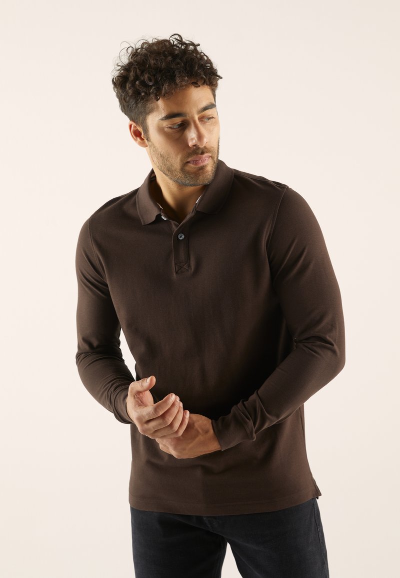 Polo à manches longues marron en tissu doux. Présente un col classique, une patte de boutonnage à un seul bouton et un design minimaliste sans motifs.