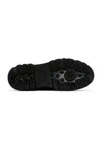 Suela de zapato de goma negra con tacos y patrones, incluyendo flechas y estrellas. Superficie texturizada con acentos elevados y una sección central lisa.