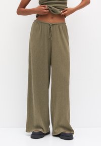 Pantalon ample vert olive en tissu côtelé. Taille élastique avec cordon de serrage ajustable. Associé à des chaussures noires sans lacets.