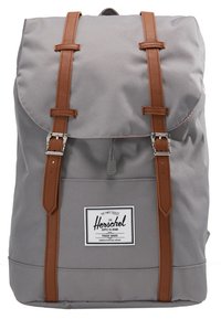 Sac à dos Herschel gris avec des sangles en cuir marron, des boucles argentées et une étiquette blanche à l'avant avec un texte noir et un logo.