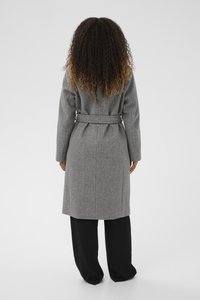 Pikk, vööga hall ülemantel, mis on valmistatud tekstuurilisest kangast, sirge lõike ja kahe külgpocketi ning kantud mustade laia säärega pükste peal.