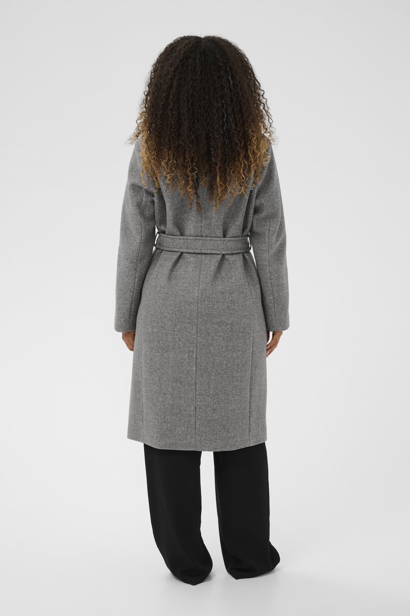 Pikk, vööga hall ülemantel, mis on valmistatud tekstuurilisest kangast, sirge lõike ja kahe külgpocketi ning kantud mustade laia säärega pükste peal.