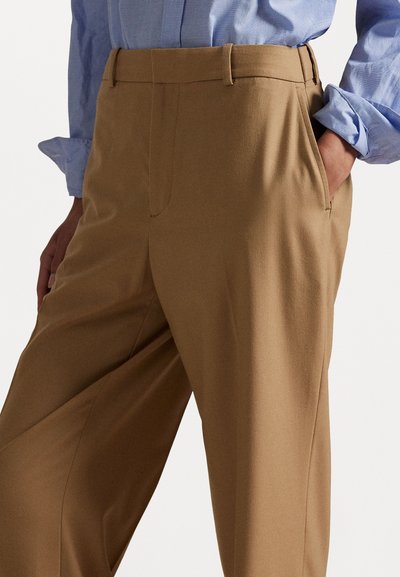 Pantalons beige ajustés avec une texture lisse, devant plissé, poches latérales et un design droit, associés à une chemise à boutons bleu clair.