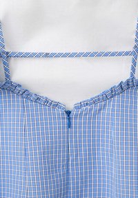 Robe sans manches à carreaux bleu et blanc avec col à volants, fermeture éclair devant et bretelles réglables sur fond blanc.