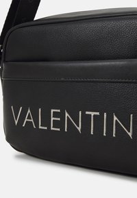 Black leather bag with textured finish, featuring silver "VALENTIN" lettering. Design is rectangular with a smooth top and seam accents.