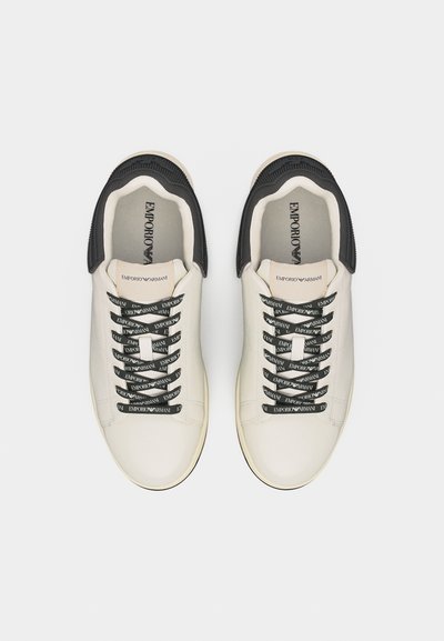 Ζευγάρι λευκά sneakers χαμηλού προφίλ με μαύρες μύτες και μαύρα κορδόνια με το λογότυπο "EMPORIO ARMANI", σε θέα από πάνω.