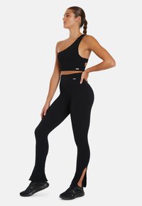 Zwarte sportoutfit met een top met één schouder en hoge taille legging met zijsplits, gemaakt van rekbare, aansluitende stof.