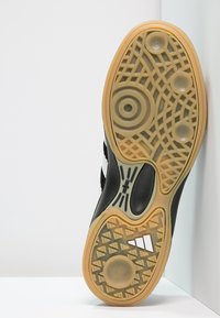 Black athletic shoe sole with a textured, patterned grip design and a light brown rubber outsole. Features circular and geometric patterns.