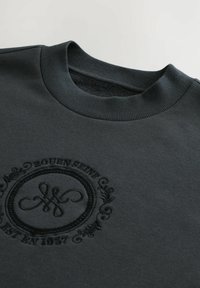 Mørkegrå sweatshirt med ribbet rund hals. Udstyret med præget cirkulært logo med teksten "Rouen Est 1857" og dekorerende detaljer. Stofblanding af bomuld.