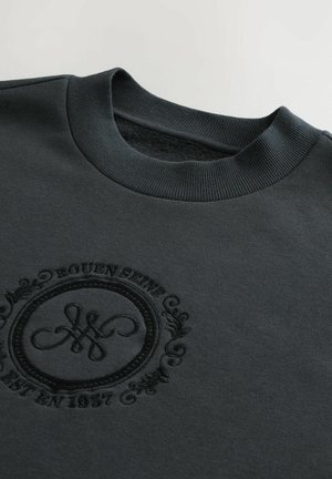 Mørkegrå sweatshirt med ribbet rund hals. Udstyret med præget cirkulært logo med teksten "Rouen Est 1857" og dekorerende detaljer. Stofblanding af bomuld.
