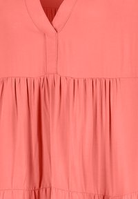 Korallenrosa Kleid mit V-Ausschnitt, gefälteltem Oberteil und fließendem Stoff. Weiche Textur mit geraffter Taille für zusätzliches Volumen.