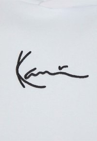 Tissu blanc avec texte en cursive noire brodée ressemblant à une signature au centre.