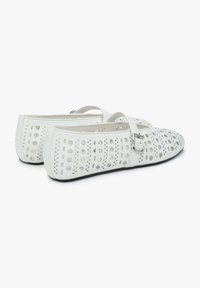 Bílé ploché boty s výřezy, se strapcem a přezkou. Materiál vypadá hladce, s klasickým, zakulaceným tvarem špičky.