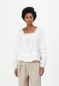 Witte blouse met groene geborduurde details langs de vierkante halslijn; lange, pofmouwen met gestreepte accenten en een losse pasvorm.