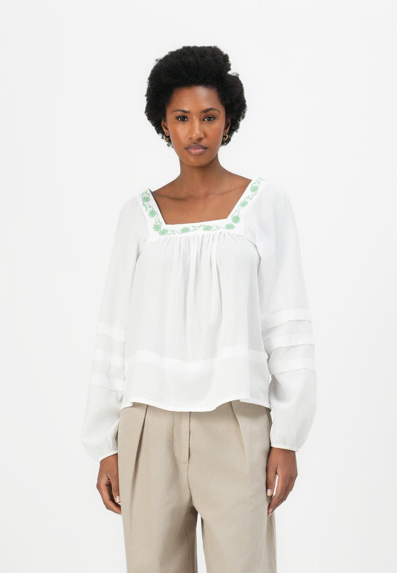 Witte blouse met groene geborduurde details langs de vierkante halslijn; lange, pofmouwen met gestreepte accenten en een losse pasvorm.