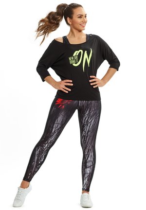 Black, oversized top with neon green text "NEW DAY BRING IT," paired with black leggings featuring floral and grass-like patterns. White sneakers.