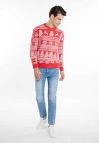 Pulover tricotat roșu cu motive festive albe, inclusiv reni și fulgi de nea. Asortat cu blugi albaștri deschiși și teniși albi.