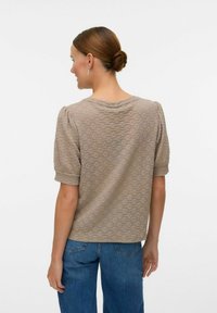 Kortärmad beige texturerad topp med ett subtilt mönster, rundad halsringning och uppvikta ärmar, kombinerad med blå denimjeans.