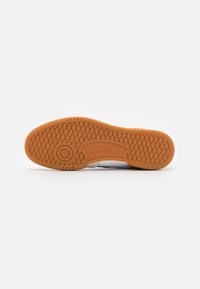 White sneaker sole with a textured orange rubber outsole, featuring a circular design element and "Reebok" logo in the center.