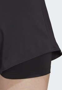 Sorte atletiske shorts med en glat overflade og en indvendig foring. Designet inkluderer et lidt længere ydre lag med en buet kant.
