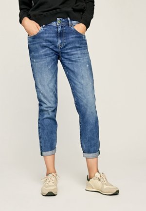 Siniset farkut mukavalla istuvuudella, käännetyt lahkeet ja hienoinen kulutus jälki. Yhdistetty vaaleanvärisiin lenkkikenkiin.