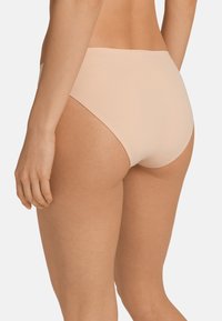 Mutande hipster seamless di un beige chiaro, con una texture liscia e morbida e un design con gamba alta, che mostra una copertura minima del tessuto sul retro.