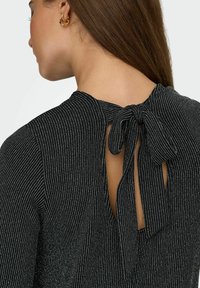 Top nero con strisce verticali argentate, presenta una schiena con apertura a chiave e un dettaglio a fiocco annodato al collo. Tessuto liscio e design aderente.