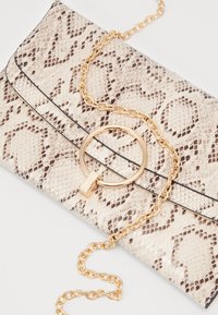 Beige ja pruun nahktekstuuriga klamber koos kuldse ümmarguse klambri ja kuldse kett käepidemega valgel taustal.