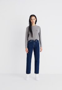 Grå langermet skjorte med logo, høyt liv mørkeblå jeans og hvite sneakers. Enkel design, rett passform og minimalistisk stil.