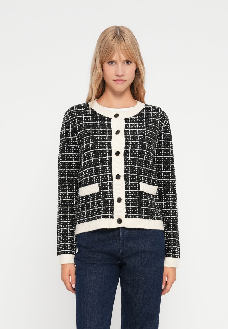 Μαύρη και λευκή καρό ζακέτα με ριχτές κρεμ λεπτομέρειες, στρογγυλή λαιμόκοψη, κουμπωτή μπροστά και δύο παPatch τσέπες. Μαλακή πλέξη.