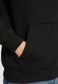 Zwarte hoodie met een geribde manchetten en onderrand, zijzak met zichtbare stikken en een gladde stoftextuur.