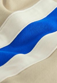 Beige fabric with a textured surface features a wavy design of white and bright blue stripes. The stitching is visible along the edges.