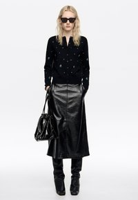 Melnas adītas kardigāns ar nelieliem dekoratīviem elementiem, kopā ar melnu ādas midi svārku. Aksesuāri ietver melnu somu un pieguļošas zābakus.