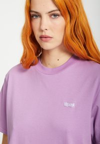 T-shirt en coton violet avec un petit logo brodé blanc. Manches courtes, col rond et texture lisse.