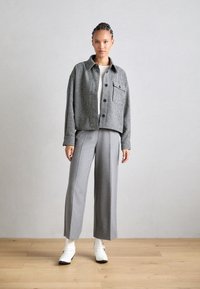 Checkered black and white jacket with a chest pocket, paired with light gray wide-leg trousers and white shoes. Smooth fabric texture.