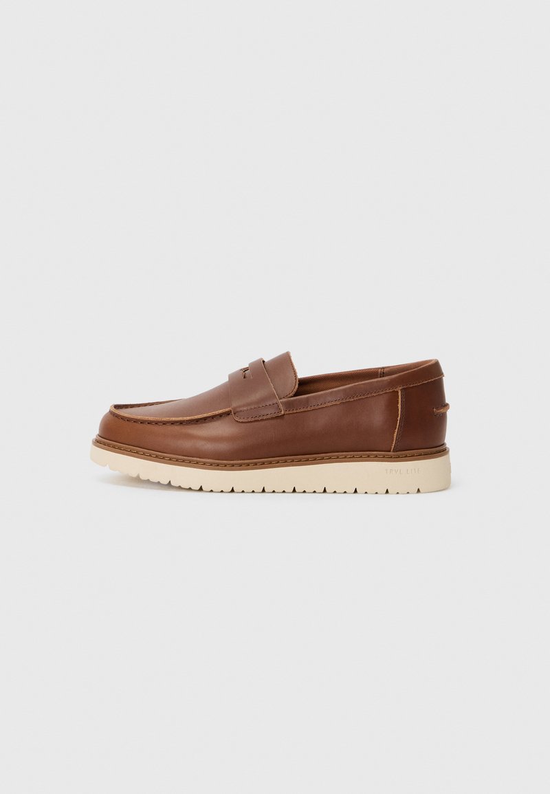 Zapato marrón de cuero tipo slip-on con parte superior texturizada, suela de goma crema y un sutil detalle de costura a lo largo de las costuras.
