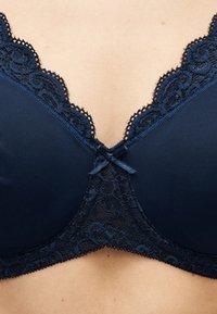 Gros plan sur la poitrine d'une femme portant un soutien-gorge bleu marine avec un bord en dentelle et un petit nœud central.