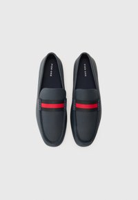 Morski slip-on cipele izrađene od teksturiranog kože s kontrastnim crnim i crvenim prugastim detaljom preko gornjeg dijela. Imaju okrugli vrh i šivani detalj.