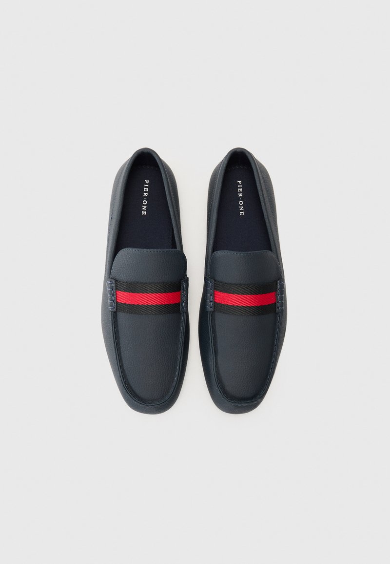 Zapatos tipo slip-on en color navy, hechos de cuero texturizado con un acento a rayas en negro y rojo que contrasta a lo largo de la parte superior. Presenta una punta redondeada y detalles de costura.