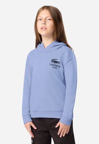 Felpa leggera blu chiaro in morbido tessuto, dotata di tasca a marsupio, polsini a costine e logo Lacoste nero sul petto.