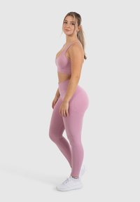 Top sportivo rosa a maniche corte e leggings a vita alta, tessuto morbido, design attillato, con motivi delicati, abbinato a scarpe sportive bianche.