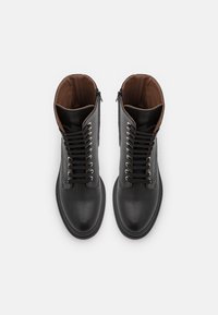 Černé kožené kotníkové boty s texturovaným povrchem, s hnědým podšívkou, kovovými očky a šňůrkami na přední straně. Zipp po straně pro zavírání.