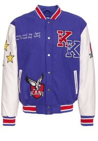 Lila varsityjacka med vita ärmar, prydd med broderade stjärnor, ett stort örn-emblem och textdetaljer i kursiv. Röda och blå accenter.