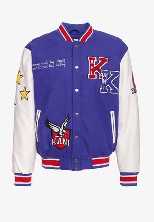 Fioletowa kurtka varsity z białymi rękawami, z haftowanymi gwiazdami, dużym emblematem orła oraz szczegółami tekstowymi w kursywie. Czerwone i niebieskie akcenty.