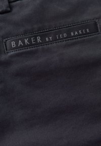 Primer plano de tela negra con etiqueta cosida que dice "BAKER BY TED BAKER" en letras mayúsculas grises.