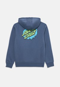 Kék anyagú kapucnis felső, amelyen egy nagy, színes grafika látható, zöld és kék "Santa Cruz Skateboards" felirattal a hátsó részen.
