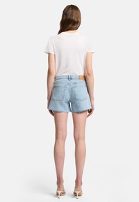 Ljus denimshorts med fransad fåll, två bakfickor och ett brunt läderpatch i midjan. I kombination med en enkel vit t-shirt.